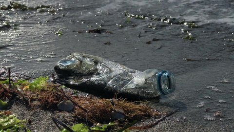 A plastic bottle lies on the beach and pollutes the sea and the life of marine life.