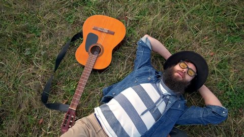 Modern young man lying on grass and holding acoustic guitar. top view