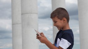 Boy in a blue T-shirt prints a message on a mobile phone and smiles