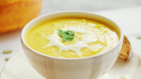 Yellow creamy pumpkin soup in bowl with pieces of bread surrounded by pumpkins on wooden table