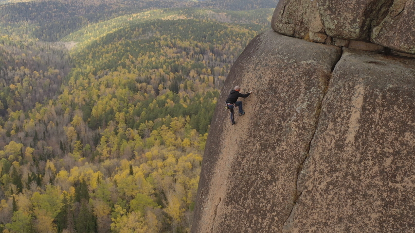 A man climbs a rock with a wonderful view of the autumn forest.