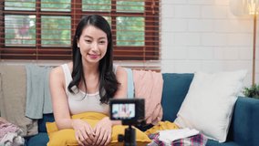 Asian stylist fashion influencer designer women using camera streaming and live to sell clothes, product, and accessories business, e-commerce broadcast online on sofa in living room at home.