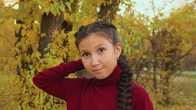 Girl holding maple leaf and pretending to be princess. Beautiful teenage girl in maroon sweater holding yellow leaf in autumn forest
