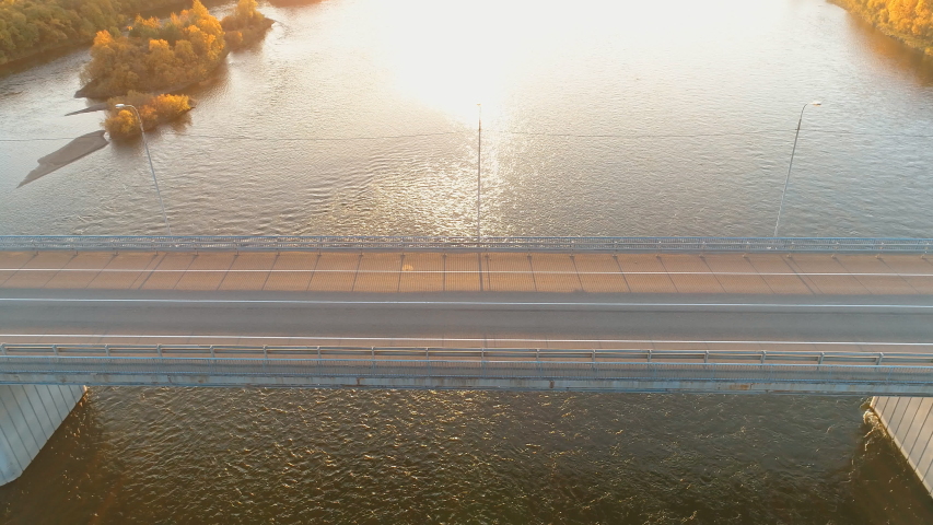 Aerial shot of a bridge with riding cars above river in autumn. yellow trees. sun shining brightly. business or family trip. car transportation. sun shines brightly
