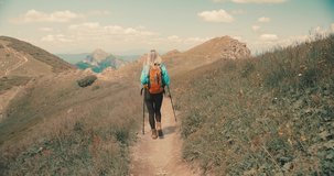 Woman backpacker tourist traveler camper walking on the top of mountain in summer sunny day under sun light. Beautiful mountains landscape view. 4K slow motion video
