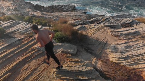 Aerial Drone Shot of Athletic Man Running on Ocean Cliffs at Sunrise with Tilt
