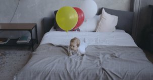 Caucasian baby laying on bed and playing with balloons in her hand. RAW Graded footage 4K slow motion 50fps 