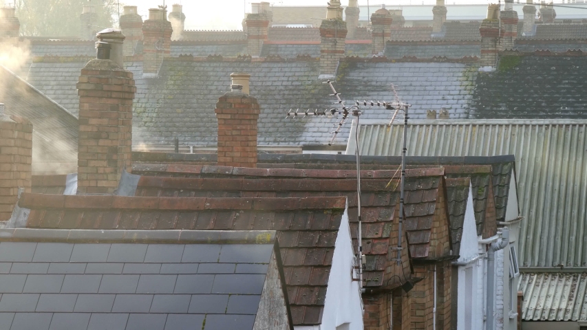 English terraced houses roof tops wall gables with slate & tiles roofs, brick chimneys, tv aerials, cold winter morning with steam rising from heating vents appears as smoke, sunny Royalty-Free Stock Footage #1040833280