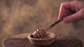 Honey dripping, pouring from honey dipper in wooden bowl. Close-up. 4K UHD video footage.
