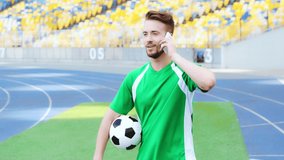 smiling footballer holding ball and talking on smartphone