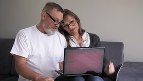Happy senior middle aged couple laughing talking embracing using laptop together looking at computer screen, making online call at home