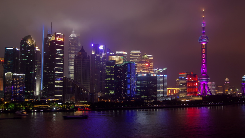 Timelapse flashing Chinese advertisements on Pudong New Area skyscrapers by TV tower reflected in Huangpu river water in Shanghai at dark night