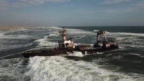 4K aerial drone video view of Namibian Atlantic coastline, Zeila L-758 Walvis Bay stranded rusty shipwreck at sand beach in Skeleton Coast Park landscape with ocean background at Namibia's west coast