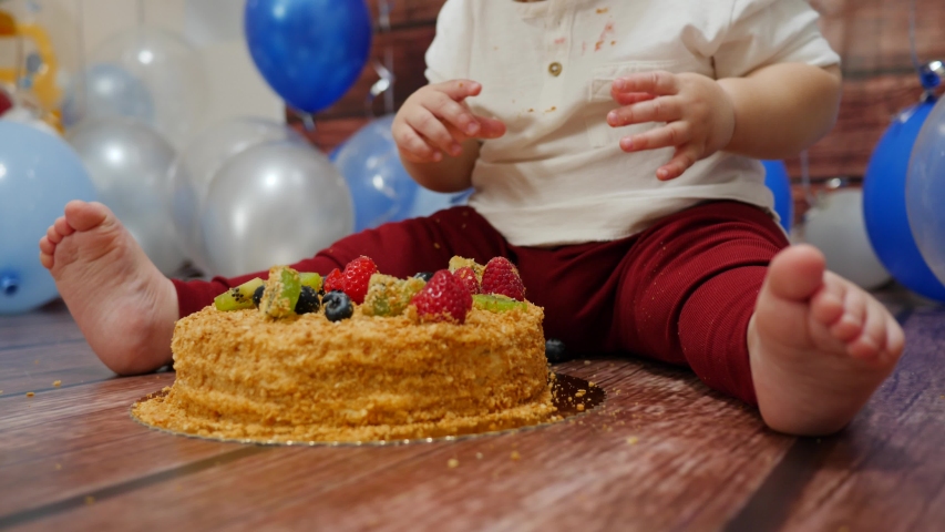 Food stained baby face eat with fingers a sweet birthday cake on a floor with berries topping celebrating 1 year