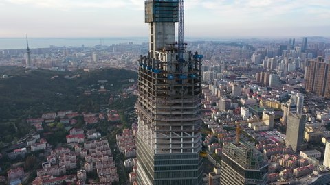 QINGDAO, CHINA – SEPTEMBER 2019: Rotating aerial view of massive construction site of skyscraper in central business district of Qingdao, with low-rise residential neighborhood in background