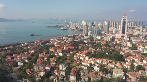 Ascending high angle drone flight of classic European (German) low-rise buildings towards more modern city center of Qingdao in China