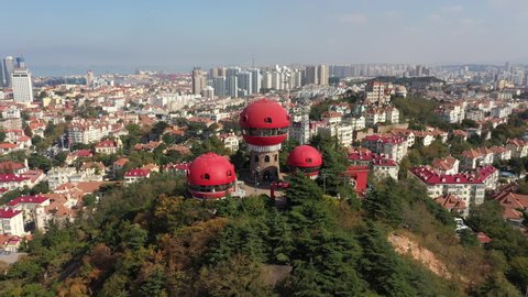 QINGDAO, CHINA – SEPTEMBER 2019: Rotating drone flight of peculiar circular shaped red observation towers on hilltop park, contrasting with colonial era architecture in Qingdao, China