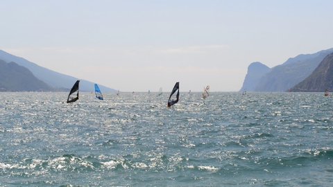 Windsurfing and paddleboarding on Lake Garda in Torbole resort. Windsurfer Surfing The Wind On Waves, Recreational Water Sports