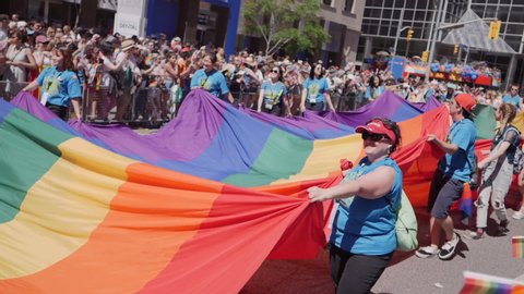 TORONTO, CANADA JUNE 23RD, 2019: Pride Protesters hold giant gay pride rainbow flag in front of cheering crowd 