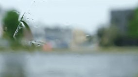 Blurred vehicles drive under rain behind wet glass in slow motion