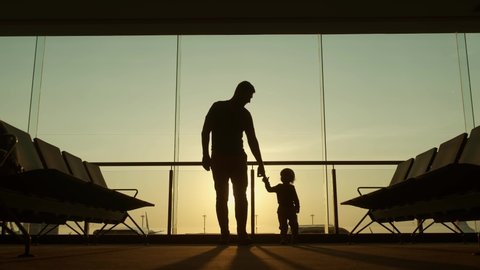 Silhouette of father and his little kid waiting for departure walking around in airport lounge room together before vacation - family, adventure concept 4k footage