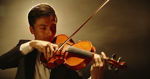 Experienced Violinist performing amazing solo on stage, spotted by light on black background close up 4k footage