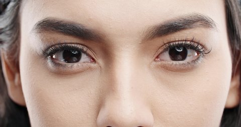 Close up shot of female eyes with makeup on eyelashes and dark brown irises looking around, isolated on black background 4k footage