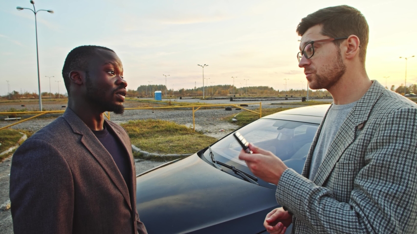 Caucasian salesman in suit talking with african business rich man customer discussing about nice car shaking hands giving keys agreeing to puchase. Car dealership.