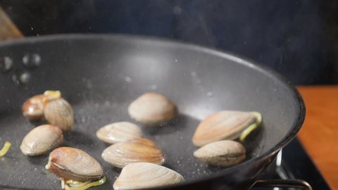Closeup shot of chef hands cooking mussels in shells tossing, mixing and throwing on pan., seafood being cooked in frying pan at restaurant kitchen, Pasta with seafood. Slow motion. Shot in hd