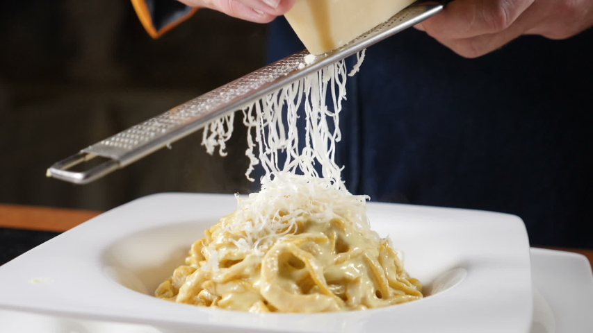 Foodvideo footage shot in slow motion. Cheese is being grated on the plate of freshly-cooked Italian pasta. Chef grating hard cheese. Cooking seafood pasta. Shot in hd | Shutterstock HD Video #1040891384
