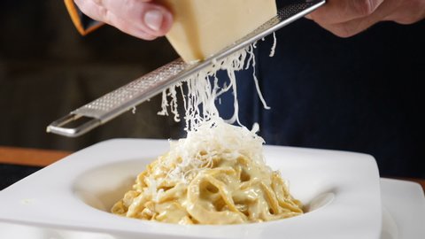 Foodvideo footage shot in slow motion. Cheese is being grated on the plate of freshly-cooked Italian pasta. Chef grating hard cheese. Cooking seafood pasta. Shot in hd