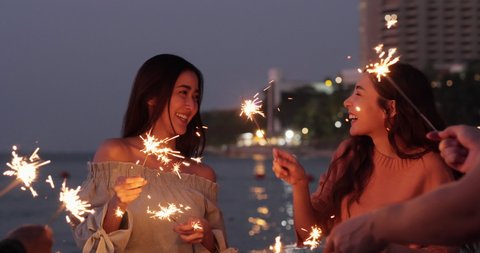 Beautiful Young woman and her friend playing sparklers dance on beach with ocean background.