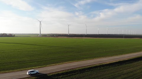 Aerial photography. white car moves on a road with a beautiful landscape. Green field and wind farms or wind turbines. Top view. Shooting from a drone or quadrocopter. Traffic on highway.