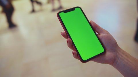 Female hand holding a smartphone with green display at a train station close-up. NYC, USA 2019