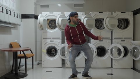 Man Dancing Viral Dance And Have Fun In the Laundry Room. Happy Guy Enjoying Dance, Having Fun Together, Party. Joyful Man With beard in Cap and Glasses Dancing Cheerful In Laundry Room.