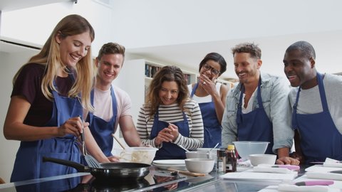 Female Teacher Making Flatbread On Cooker In Cookery Class As Adult Students Look On