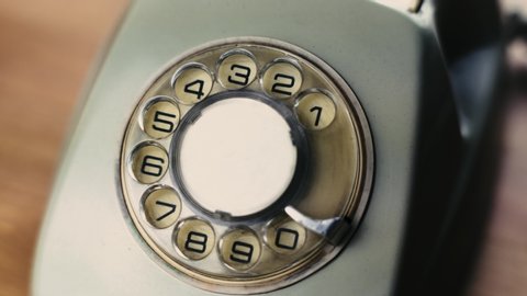 Close-up view on an old style telephone dial. Antique white telephone. Rotating all numbers by finger. Old fashioned. Classic phone.