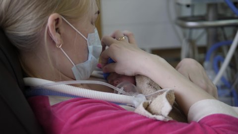 A woman in a medical mask is holding a newborn baby