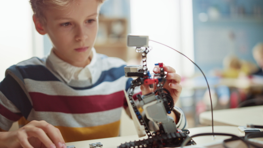 Smart Schoolboy Builds / Constructs Small Robot and Uses Laptop to Program Software for Robotics Engineering Class. Elementary School Science Classroom with Gifted Brilliant Children with Technology Royalty-Free Stock Footage #1040916677
