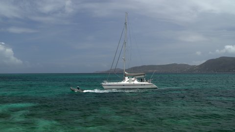 Distant motorboat leaving catamaran in ocean near island / St. Vincent and the Grenadines