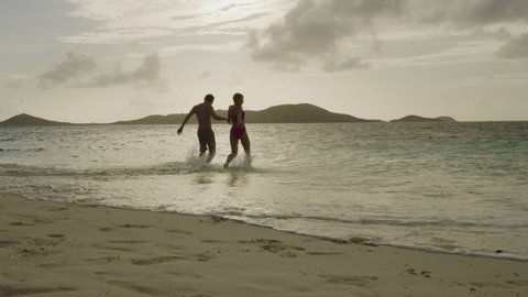 Slow motion of couple holding hands and running on beach into ocean / Jamesby Island, Tobago Cays, St. Vincent and the Grenadines