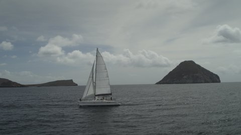 Panning shot of distant catamaran in ocean near island / Ronde Island, Grenada