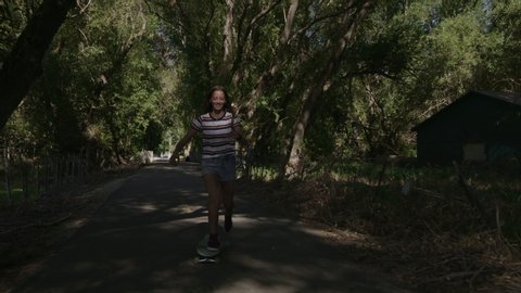 Tracking shot of happy girl riding skateboard on park path / Saratoga Springs, Utah, United States