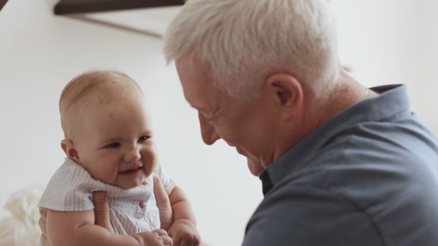 Funny Games and Laugh of Caucasian Old Man and Baby Kid in Domestic Comfort. Wrinkled Skin of Grandfather or Gray Haired Parent in Casual Day Light. Gentle Embrace and Happy Smile of 60s Grandparent Royalty-Free Stock Footage #1040923406