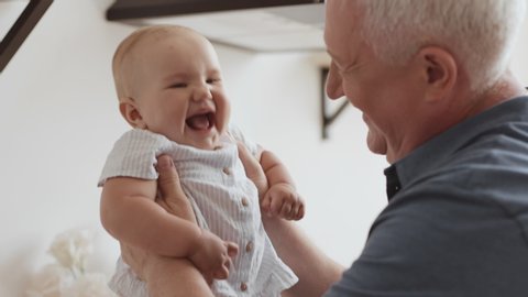 Funny Games and Laugh of Caucasian Old Man and Baby Kid in Domestic Comfort. Wrinkled Skin of Grandfather or Gray Haired Parent in Casual Day Light. Gentle Embrace and Happy Smile of 60s Grandparent