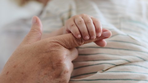 Family Relation of Elder Grandmother and Happy Grandchild. Hand of Carefree Son Holding Finger of Caucasian 60s Woman. Happiness of Parent and Newborn Baby at Comfortable Home in Day Lighting Indoors