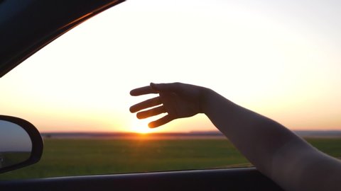 A young girl put her hand out of the car window at sunset. Close up.Slow motion. Summer travel by car. Girl on vacation, family travel. Girl's hand at sunset