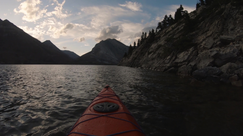Kayaking in Glacier Lake surrounded by the beautiful Canadian Rocky Mountains during a cloudy summer sunset. Taken in Upper Waterton Lake, Alberta, Canada.