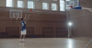 A professional videographer taking video shots of basketball afro-american man on training in gym. Black guy with ball playing on playground. Slow motion 4k raw footage 60 fps