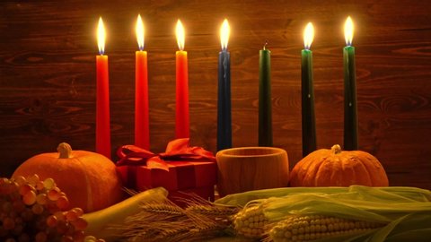 ignition of Kwanzaa traditional candles, festival concept with gift box, pumpkin, ears of wheat, grapes, corns, banana, bowl and fruits on wooden background